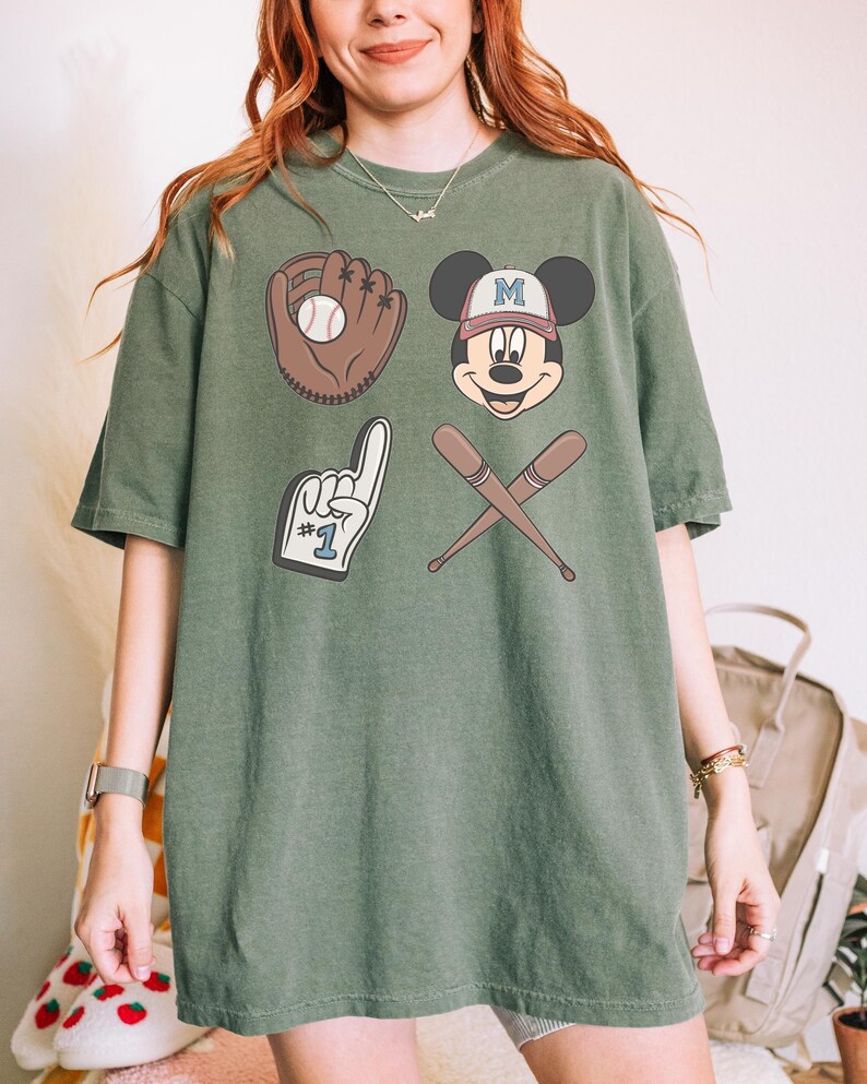 May include: A green t-shirt with a baseball theme featuring Mickey Mouse wearing a baseball cap with the letter "M" on it, a baseball glove with a ball, a baseball bat and a foam finger with the number "1" on it.