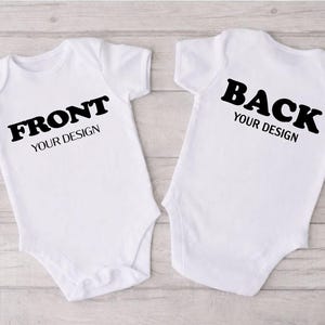 two white baby onesies with black text on the back, placed side by side on a wooden surface.