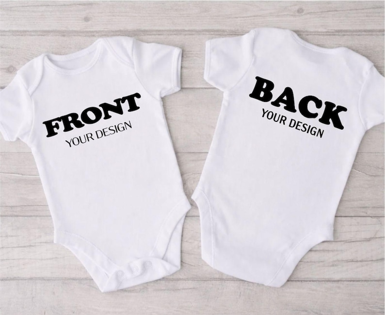 two white baby onesies with black text on the back, placed side by side on a wooden surface.