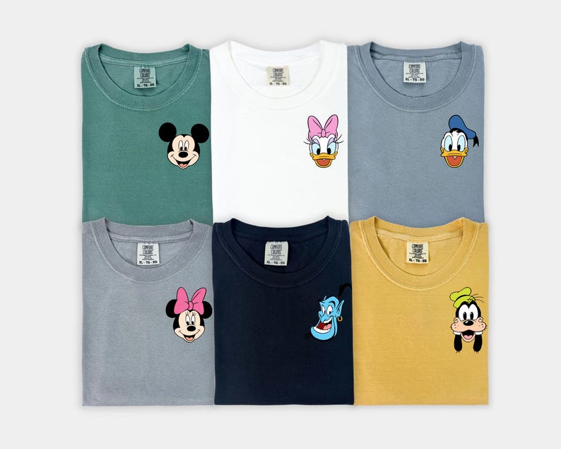 May include: Six t-shirts in various colors, each featuring a different Disney character graphic on the chest. The characters include Mickey Mouse, Daisy Duck, Donald Duck, Minnie Mouse, Genie, and Goofy. The shirts are folded and displayed on a white surface.