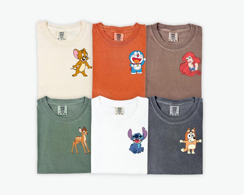 May include: Six folded t-shirts in various colors, each featuring a cartoon character on the front. Colors include cream, orange, brown, green, white, and charcoal. Characters include Jerry, Doraemon, Ariel, Bambi, Stitch, and Bluey.