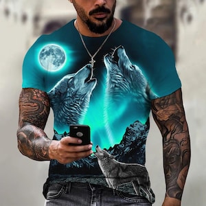 May include: Teal crew neck t-shirt with a wolf howling at the moon design. The graphic includes a full moon, mountains, and a third wolf. The shirt has a teal and blue gradient colour scheme.