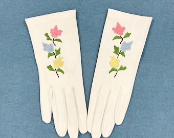 May include: A pair of white gloves with embroidered flowers in pink, yellow, blue, and green.