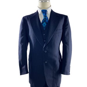 May include: A navy blue pinstripe suit with a three-piece design, including a jacket, vest, and trousers. The suit features a white dress shirt and a patterned blue tie. The suit is displayed on a mannequin.