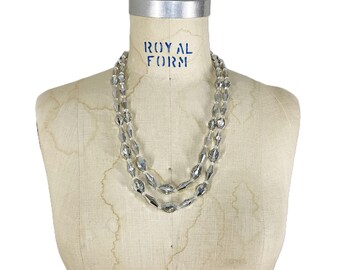 May include: A vintage, two-strand necklace with clear, faceted beads. The necklace is draped on a vintage dress form. The dress form has the words "ROYAL FORM" printed on it in blue letters.
