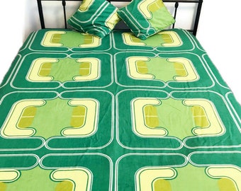 May include: Green and yellow geometric patterned bedspread with two matching pillowcases. The bedspread has a repeating pattern of squares with rounded corners and a curved line design.