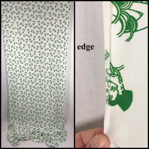 May include: White fabric featuring a repeating pattern of green floral designs. The fabric is draped, displaying the pattern's coverage. A close-up shows the fabric's edge, highlighting the material's texture and the green floral design.