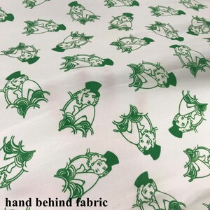 May include: White fabric featuring a repeating pattern of green illustrations. Each illustration shows a person in a top hat and a decorative design. The fabric has a soft, slightly textured appearance.
