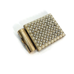 May include: A gold-toned compact with a hinged mirror and a lipstick tube. The compact is covered in a pattern of faux pearls and rhinestones.