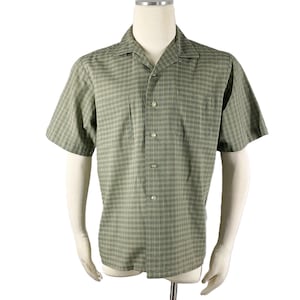 Peut inclure: Une chemise à manches courtes à carreaux verts et beiges. La chemise a un col chemise, deux poches poitrine et est présentée sur un mannequin. Le tissu est léger.