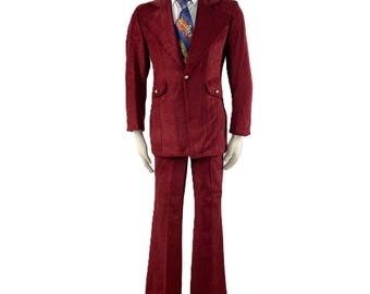 May include: A burgundy corduroy suit displayed on a mannequin. The suit includes a two-button jacket with pocket flaps and flared pants. A patterned tie and white dress shirt are visible.