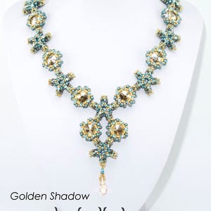 Könnte beinhalten: Eine türkisfarbene und goldene Perlenkette mit einem Tropfenanhänger. Die Kette heißt "Golden Shadow" und wurde von Isabella Lam entworfen. Der Text "REEF necklace" befindet sich oben im Bild.