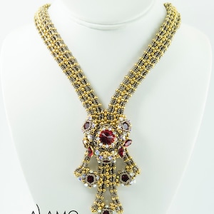 Könnte beinhalten: Eine goldene und silberne Perlenkette mit einem roten Kristall-Anhänger. Der Anhänger besteht aus mehreren Schichten von Perlen und Kristallen, die einen kaskadierenden Effekt erzeugen. Die Kette wird auf einer weißen Puppe präsentiert.