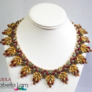 以下が含まれることがあります： 茶色、赤、金、緑のビーズを使った幾何学模様のビーズネックレス。ネックレスは白いマネキンに飾られています。