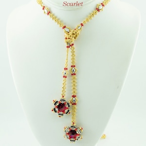 May include: A gold and red beaded lariat necklace with a red gemstone pendant. The necklace is called "Fixer Lariat" and the color is "Scarlet". The necklace is designed by Isabella Lam.