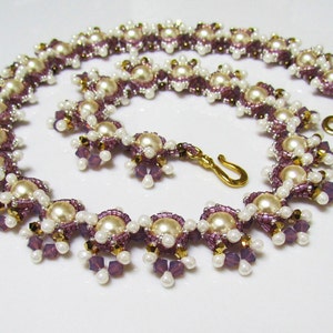 May include: A delicate necklace made with white pearls, purple crystals, and gold beads. The necklace has a simple clasp closure.