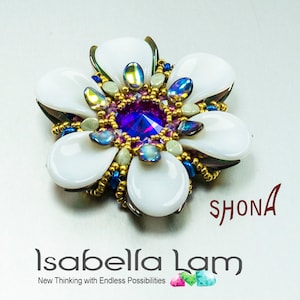 Op de afbeelding: Een witte, bloemvormige kralen broche met een paarse kristal in het midden. De broche is omgeven door iriserende kralen en gouden kralen. De tekst "SHONA" is zichtbaar in de rechterbenedenhoek van de afbeelding.