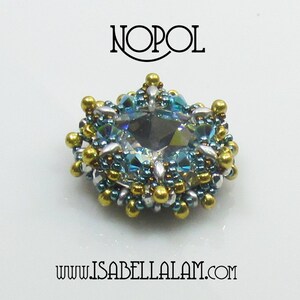 May include: A handcrafted, beaded brooch with a large, faceted, gray-blue crystal center. The brooch features a halo of teal, silver, and gold beads, with the word "NOPOL" above and "www.ISABELLALAM.com" below.