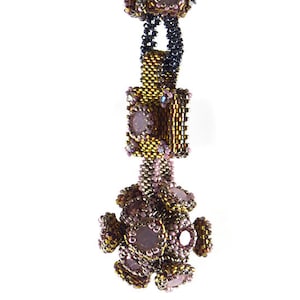 Puede incluir: Un collar de cuentas con un esquema de color dorado y rosa. El collar presenta una serie de formas geométricas y un gran colgante redondo.