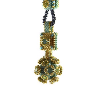 Puede incluir: Un collar de cuentas con un colgante verde y dorado. El colgante es una forma geométrica con una base cuadrada y una parte superior redonda. El collar está hecho de pequeñas cuentas redondas en tonos verdes y dorados.