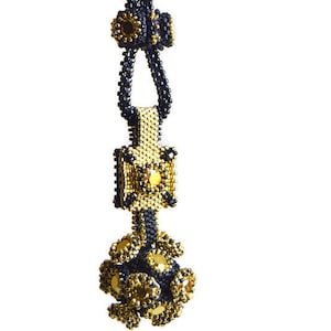 Puede incluir: Un collar de cuentas negras y doradas con un colgante geométrico y un racimo de cuentas en la parte inferior.