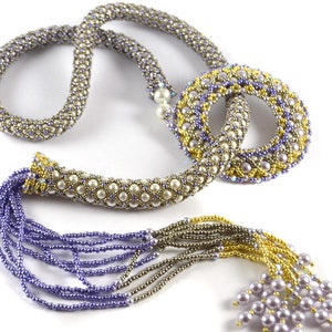 Op de afbeelding: Een kralenketting met een lange, meerstrengs kwast. De ketting is gemaakt van zilveren, gouden en paarse kralen. De kwast is gemaakt van paarse, zilveren en gouden kralen. De ketting heeft een grote, ronde hanger.