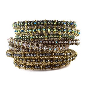 Könnte beinhalten: Ein Stapel Perlenarmbänder in Grün-, Braun- und Silbertönen. Die Armbänder sind aus kleinen, runden Perlen gefertigt und haben verschiedene Muster.