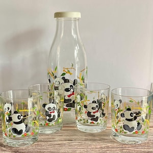 May include: A set of four clear glass tumblers and a glass bottle with a white lid. All the glasses and bottle have a panda bear design with black and white pandas on a green and yellow background.