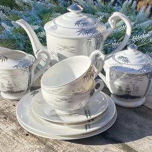 May include: A white tea set with a silver and black bamboo design. The set includes a teapot, creamer, sugar bowl, two teacups, and two saucers.