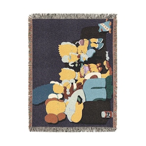 May include: A woven throw blanket featuring a dark navy background with a graphic illustration of yellow cartoon characters lounging on a black sofa. The characters have X-shaped eyes and are depicted in various poses, with a small soda can visible.