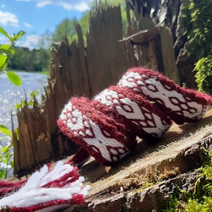 May include: A red and white woven bracelet with a geometric pattern. The bracelet is made of yarn and has a tassel.