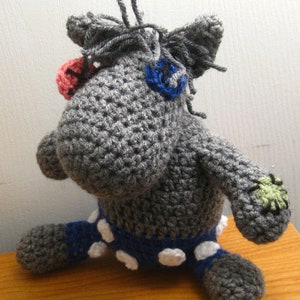 Puede incluir: Un animal de peluche gris tejido a crochet con pantalones de lunares azules y blancos. El animal tiene un hocico largo y ojos grandes.