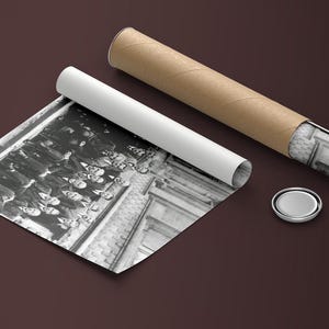 Puede incluir: Una impresi&oacute;n fotogr&aacute;fica en blanco y negro, parcialmente desenrollada, que representa a un grupo de personas. La impresi&oacute;n va acompa&ntilde;ada de un tubo blanco enrollado, un tubo de cart&oacute;n marr&oacute;n y una tapa plateada. La fotograf&iacute;a est&aacute; sobre una superficie marr&oacute;n oscuro.