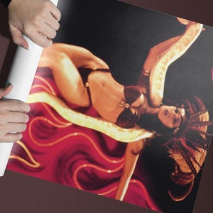 May include: A woman with long, dark hair lies on a red and gold background. She is wearing a black bikini and a gold necklace. She has a snake wrapped around her arm.