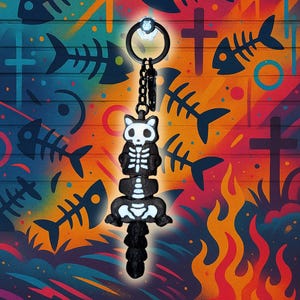 May include: A black and white skeleton cat keyring with a chain and ring. The cat is stacked on a spine and pelvis. The background is a colourful graffiti wall with fish skeletons, crosses, and flames.