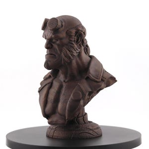 May include: A brown bust depicting a character with horns and a serious expression. The sculpture has a detailed beard and jacket, mounted on a black base. A collectible item, the bust is a detailed representation.