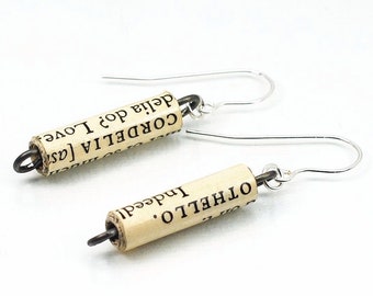 May include: A pair of silver earrings with a rolled up paper charm. The paper is printed with the text "CORDELIA" and "OTHELLO".