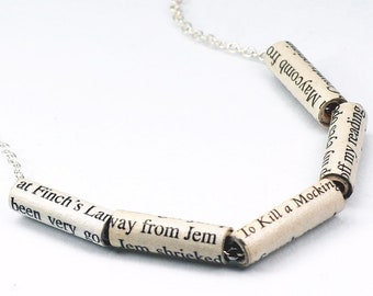 May include: A silver chain necklace with paper bead charms. The beads are made from pages of the book "To Kill a Mockingbird" and feature text from the book. The beads read "been very go Jem shrieked at Finch's Lanway from Jem To Kill a Mocking Maycomb fro County visio off my reading."