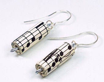 May include: A pair of silver earrings with a cylindrical charm made from rolled sheet music. The charms are decorated with black musical notes on a white background.