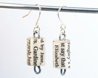 May include: A pair of cork earrings with gold hooks and silver rings. The cork is printed with text from a book, including the words "Bingley's", "Elizabeth", "Jane", and "Gardine".