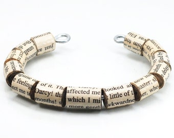 May include: A bracelet made of rolled-up pages of a book, with the text "Darcy! the which I mi" visible. The bracelet is made of cream-colored paper and has silver metal clasps.