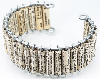 May include: A silver wire bracelet with rolled up pages of a book attached to it. The pages have text printed on them, including the words "Layamon" and "marabou".