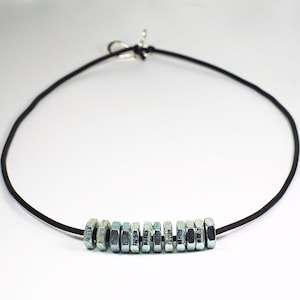May include: A black leather cord necklace with a row of silver metal hex nuts as a pendant.