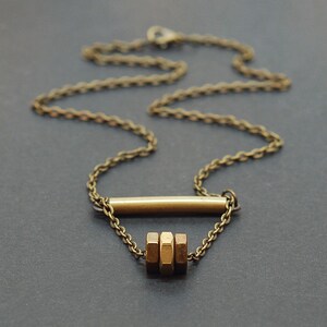 May include: A gold necklace with a simple bar pendant and a cluster of three hexagonal beads.