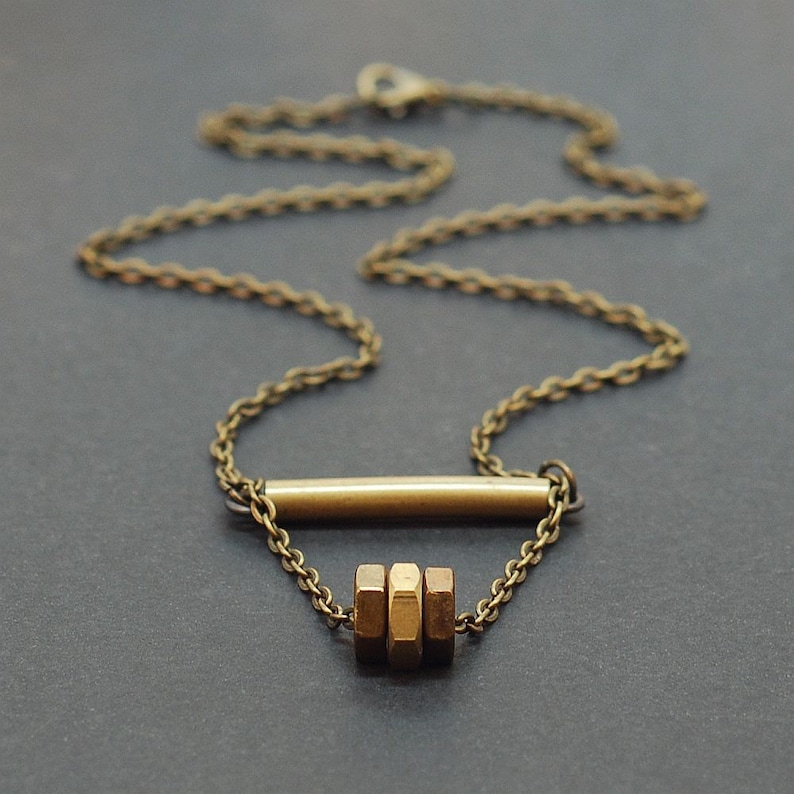 May include: A gold necklace with a simple bar pendant and a cluster of three hexagonal beads.