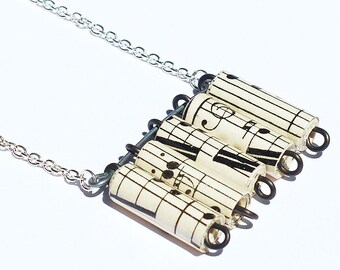 May include: A silver chain necklace with a pendant made of rolled sheet music featuring musical notes. The pendant is made of five rolled pieces of sheet music connected by wire.