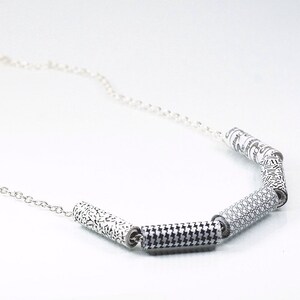 May include: A silver chain necklace with five black and white patterned cylinder beads. The beads have different geometric designs.