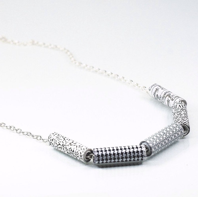 May include: A silver chain necklace with five black and white patterned cylinder beads. The beads have different geometric designs.