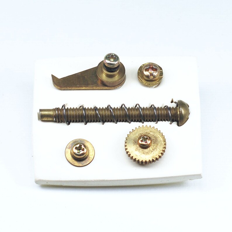 May include: A set of five brass-colored metal parts, including a spring, a gear, a hook, and two screws, displayed on a white background.