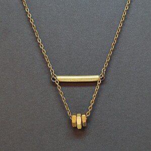 May include: A gold chain necklace with a horizontal bar pendant and a stack of three hexagonal charms.